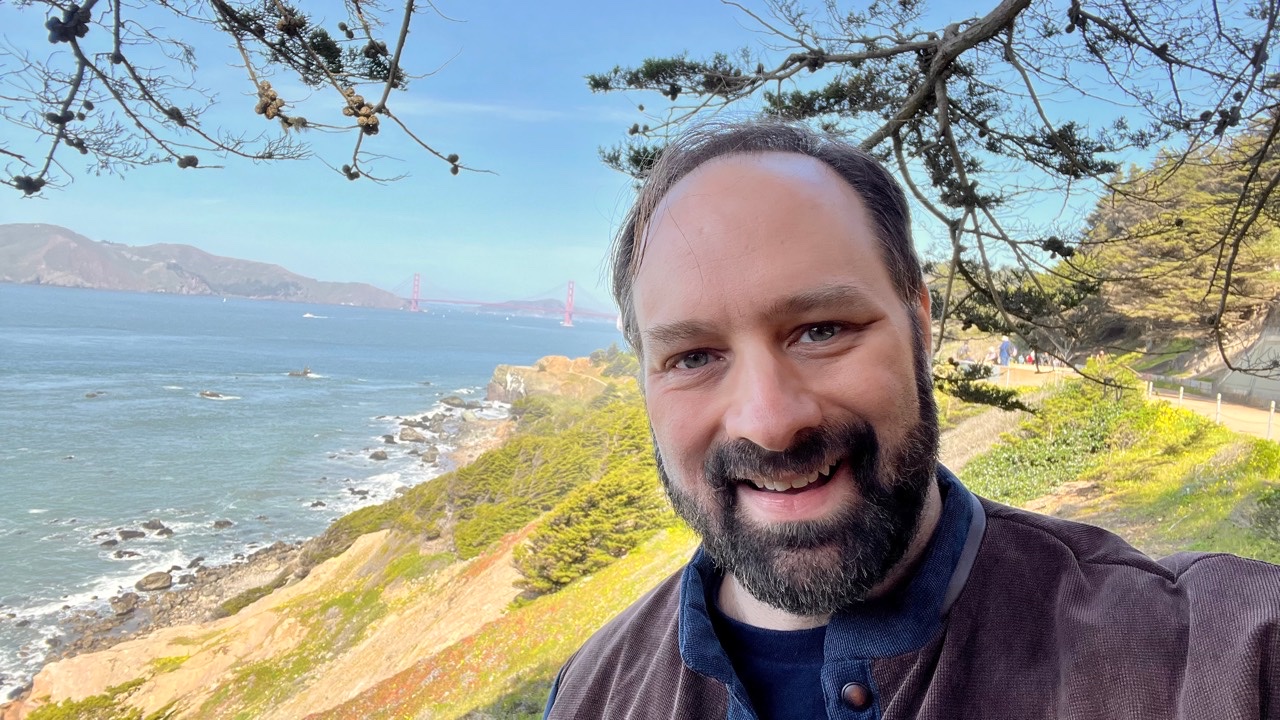 Chris Hollander smiling beside the San Francisco coast, with the Golden Gate Bridge in the distance