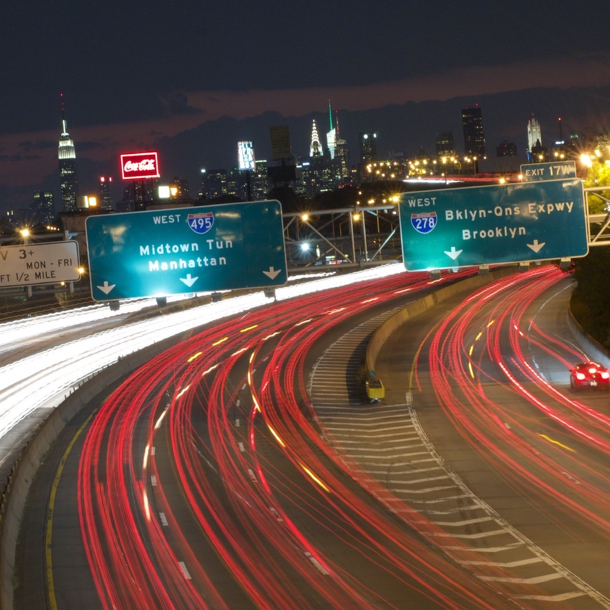 Long-exposure view of brightly lit Queens expressways and the Manhattan skyline at night
